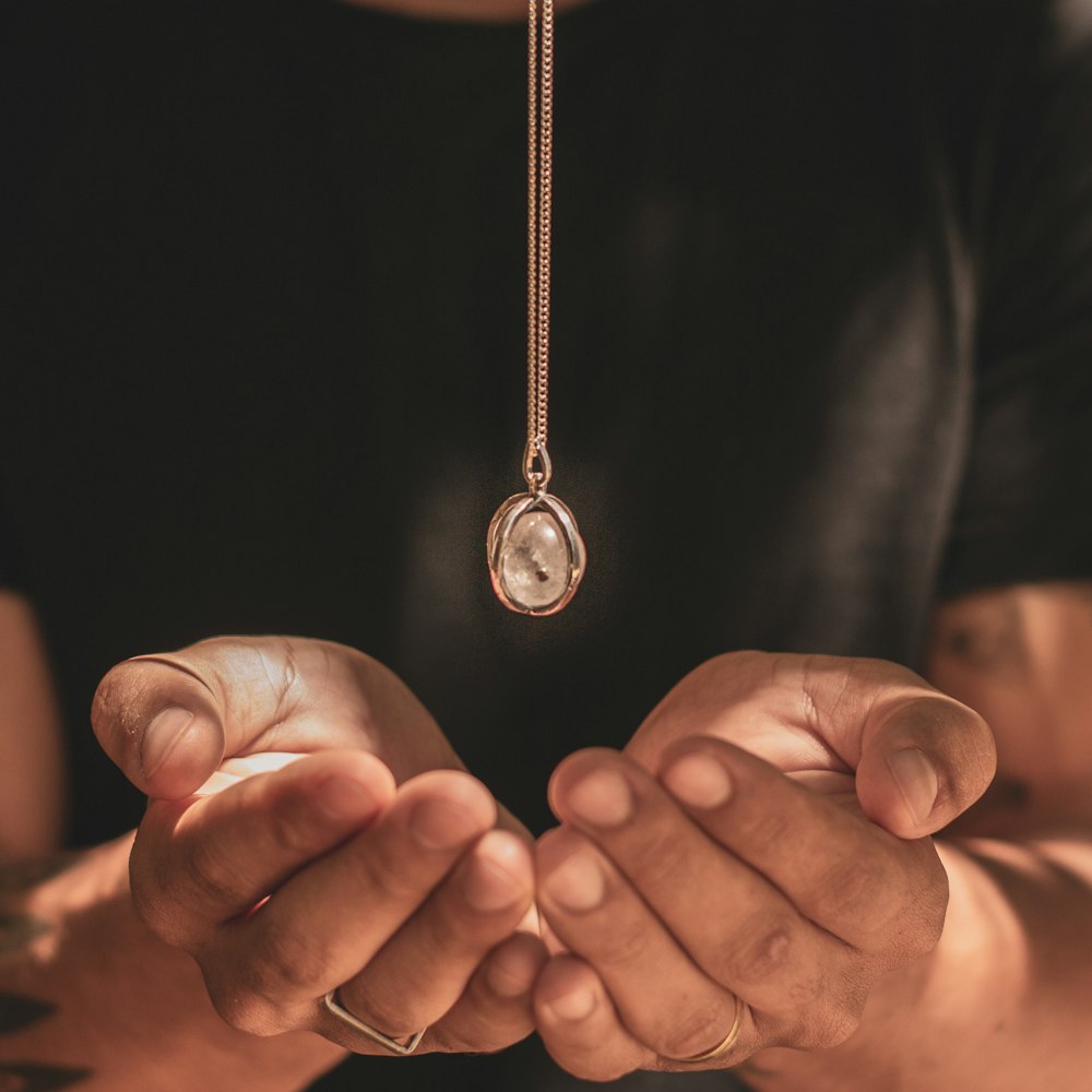 silver-colored necklace above human hand