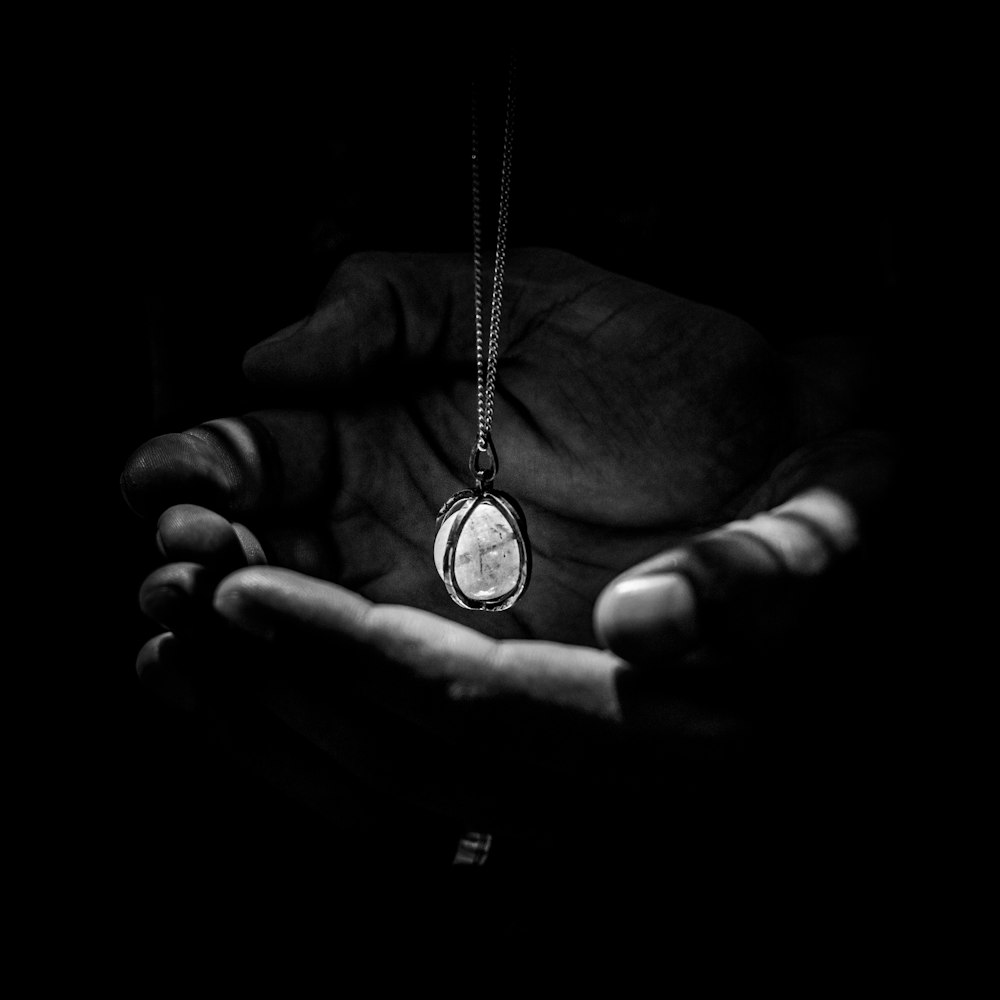 greyscape photography of pendant necklace on human hand