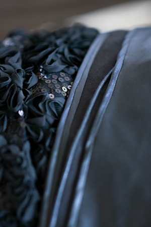 Detailed close-up of a textured fabric featuring intricate ruffles and sequins. The material appears glossy and is adorned with black embellishments arranged in a pattern.