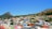 A vibrant neighborhood with brightly colored buildings nestled between two hills. The area boasts a variety of architectural styles and is rich in greenery, with trees scattered throughout. The sky is clear and blue, providing a picturesque backdrop to the lively scene.