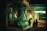A street-level view at night features the front of a tram with a reflective windshield, illuminated by nearby lights. In the background, a brightly lit sign reads 'OPTUS' from a shop. Silhouettes of people are visible walking on the sidewalk, adding a sense of movement.