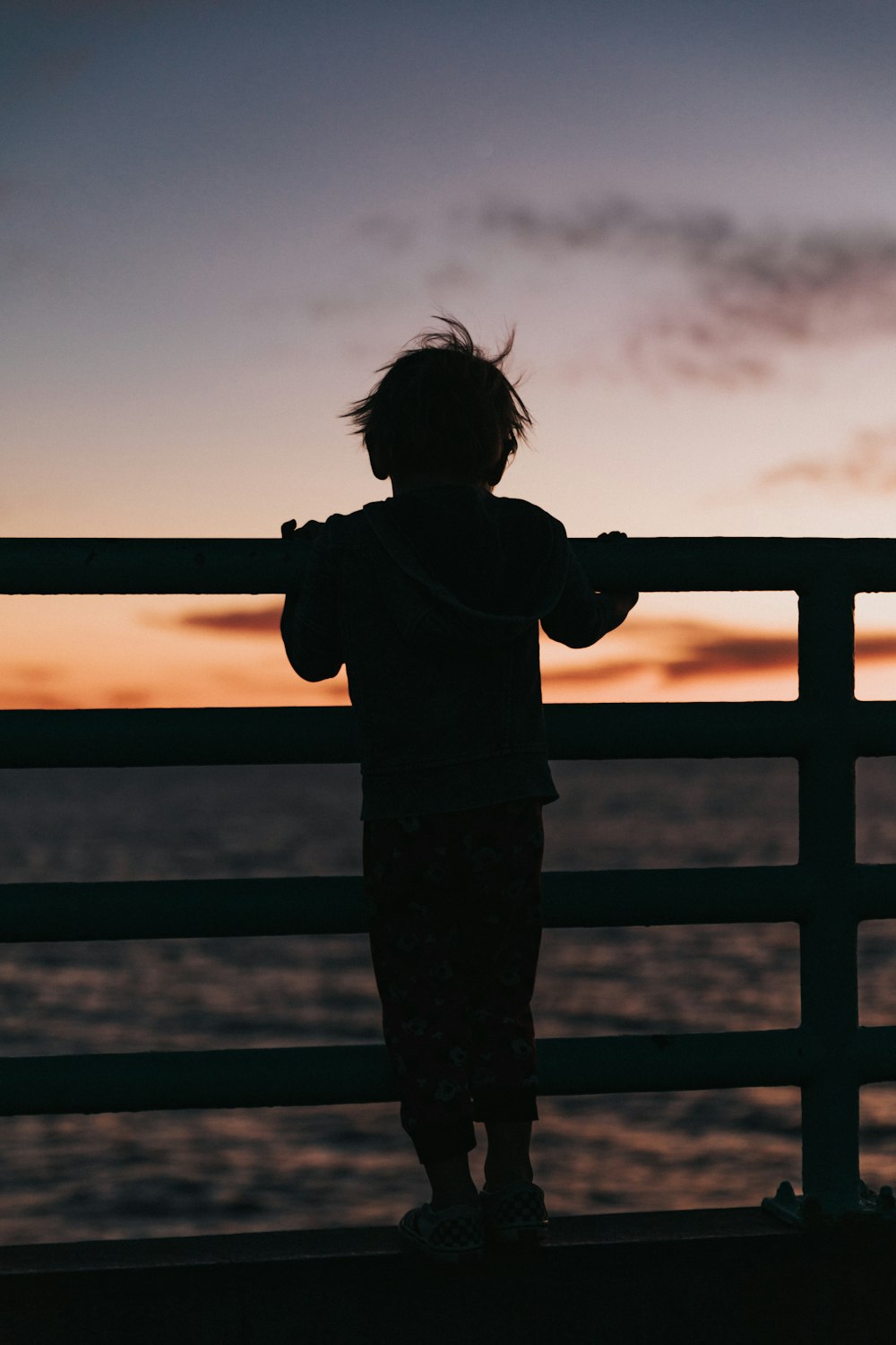 Silhouette eines Kleinkindes, das während des Sonnenuntergangs auf einem Geländer steht