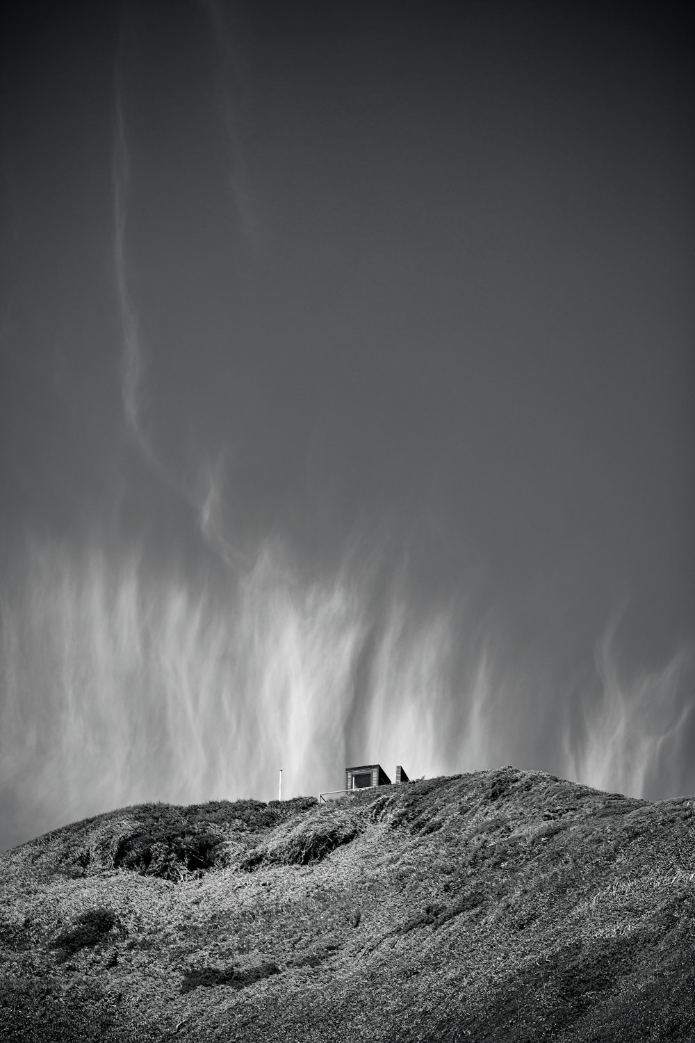 grayscale photo of house in the middle of mountain grass field