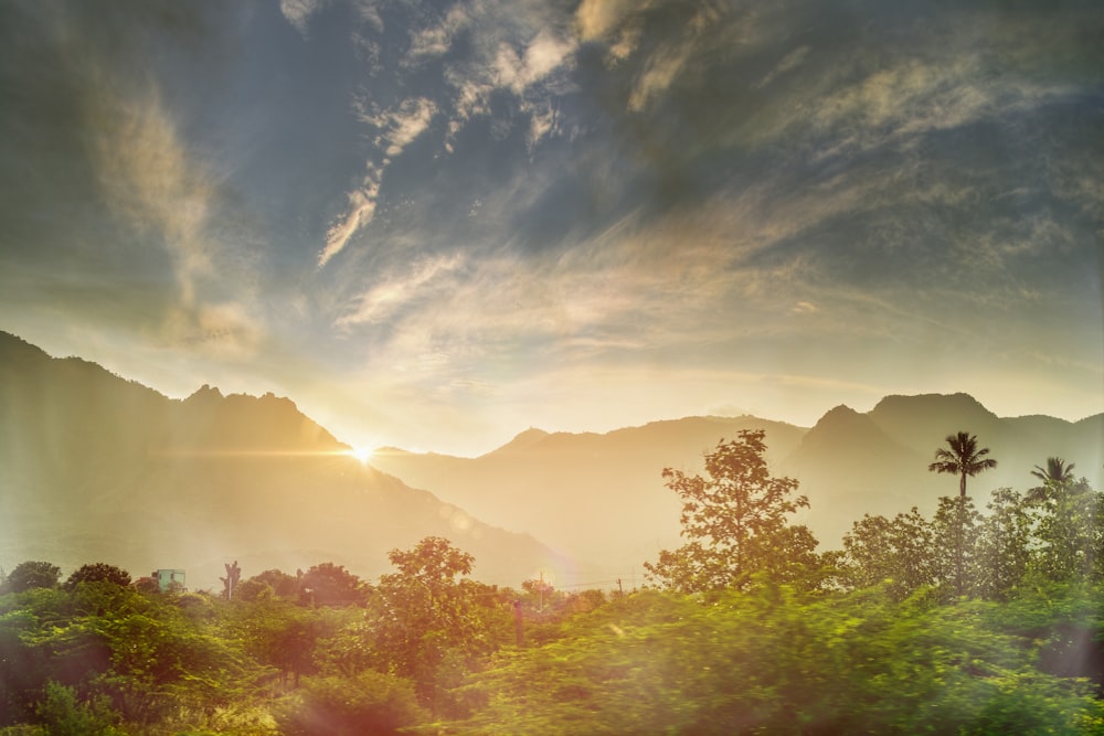 the sun is setting over the mountains and trees