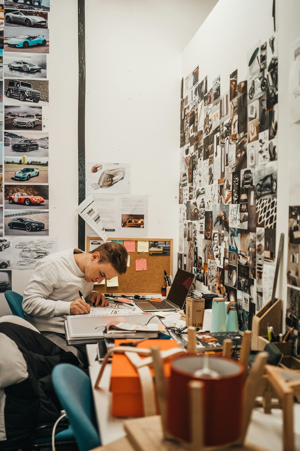 hombre escribiendo al lado de la pared con fotos de coches