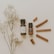 Two small bottles of essential oils are placed on a light surface, accompanied by several cinnamon sticks arranged to the right. A sprig of delicate white flowers lies on the left side, adding a natural touch to the composition.