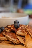 A close-up of a fluffy stack of buttermilk pancakes drizzled with maple syrup and fresh berries on top.