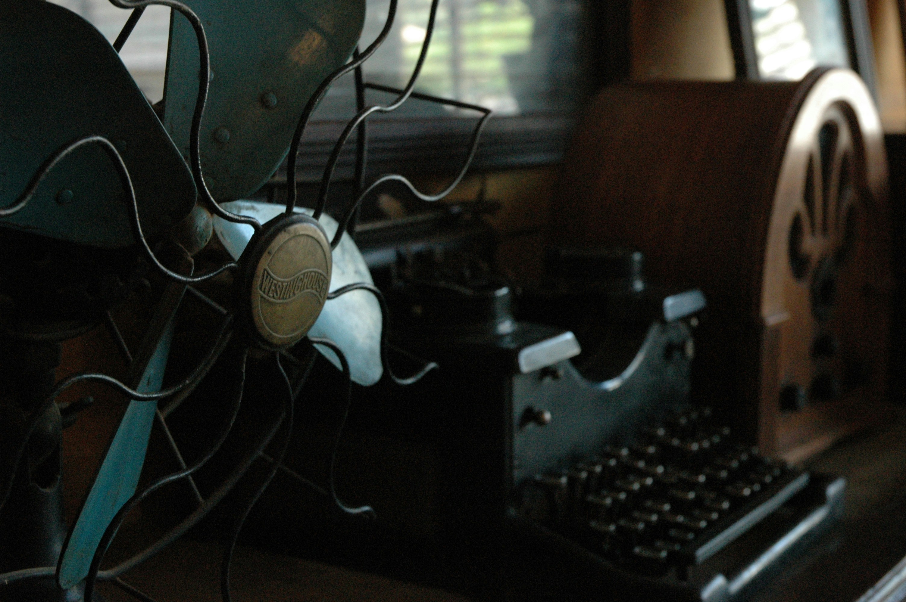 low-light photo of typewriter in between of cathedral radio and parabolic dish, Vintage Westinghouse fan, black typewriter, old radio, collection of items from the 1930