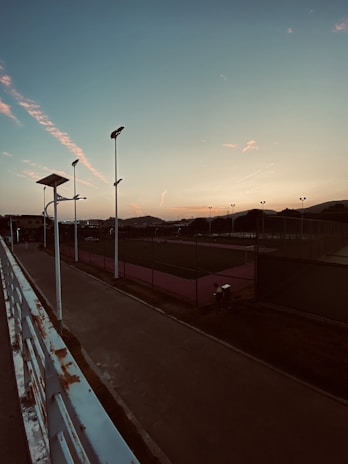 Sunset casting a warm burnt orange glow over the outdoor courts, with kids practicing shots in the background.