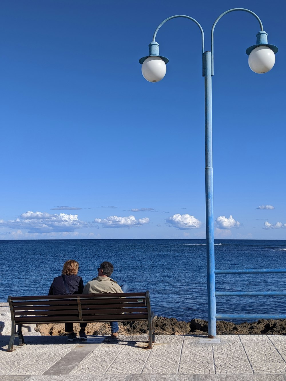 duas pessoas sentadas no banco ao lado do poste de luz azul