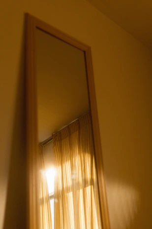A sleek modern mirror reflecting a sunlit living room with linen curtain panels gently swaying.