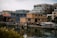 Houseboats are moored along a calm dock in front of modern apartment buildings, reflecting the urban residential setting. The water is still, and the lighting is soft, indicating a cloudy or overcast day.
