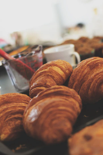 A close-up of freshly baked golden croissants stacked on a rustic wooden tray.