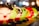 A collection of colorful, cartoonish character lamps lined up in a row. The figures feature exaggerated facial expressions and are brightly illuminated, casting a warm glow. The background is softly blurred, creating a bokeh effect with circular lights.