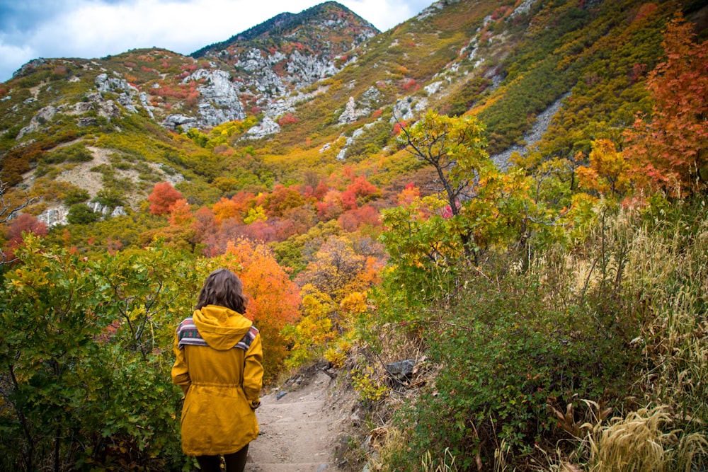 a woman in a yellow jacket walking up a trail