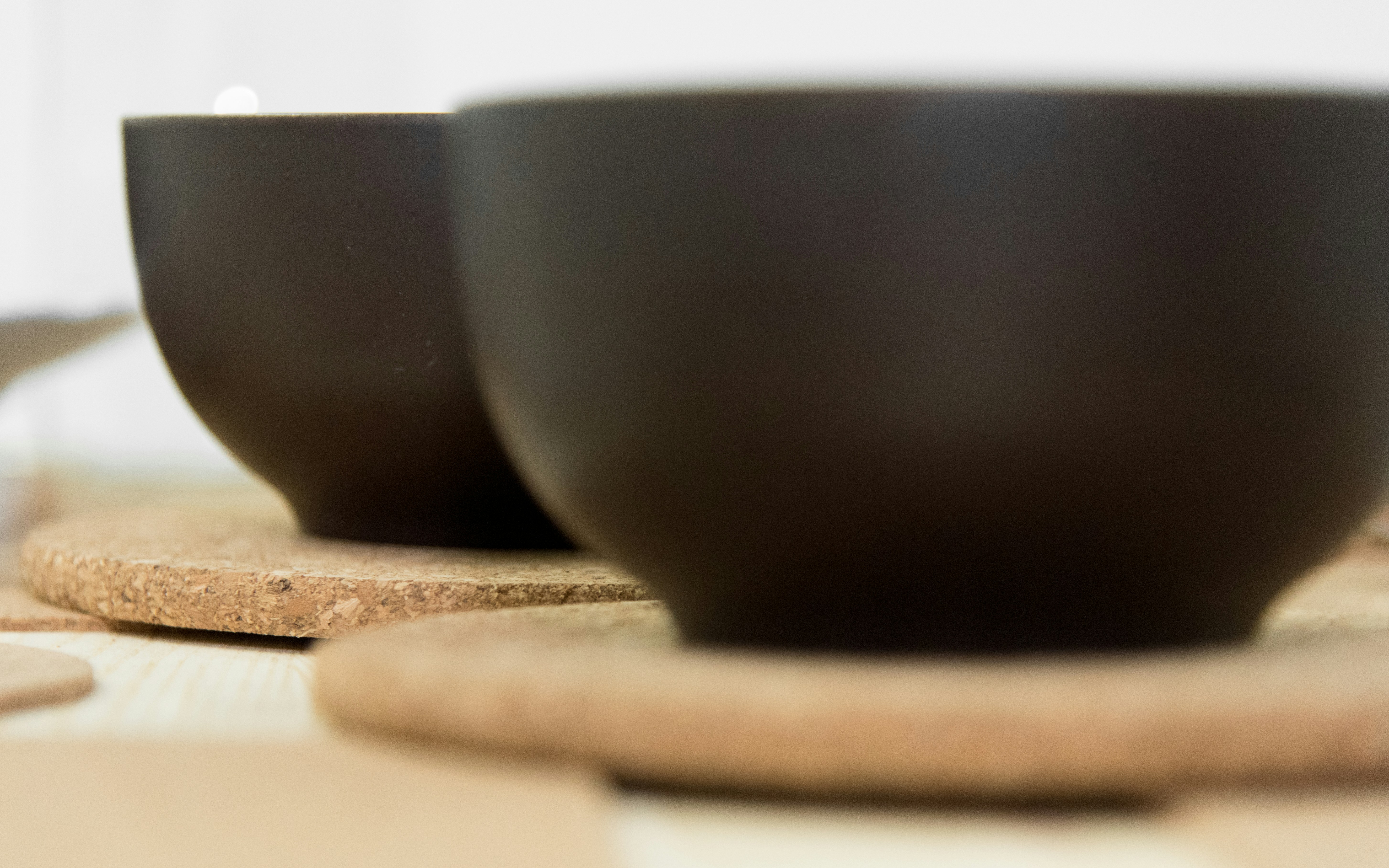 two black ceramic bowls on boards, There are 2 Black and Brown bowls on the dinning table with cork plate.