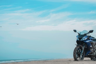 A vibrant motorcycle parked by a beach road with the sea in the background.