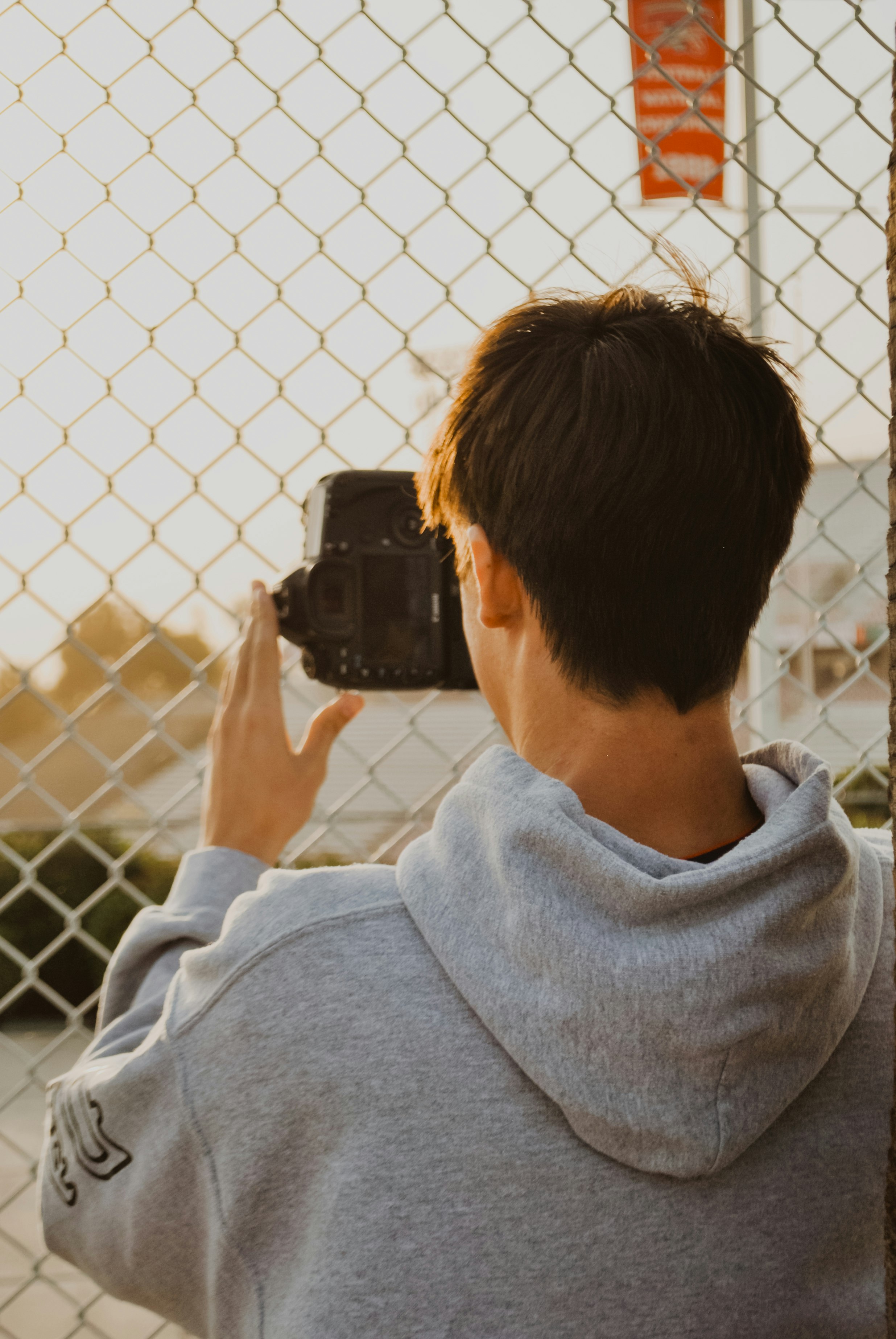 man in grey hoodie taking photo near chain link