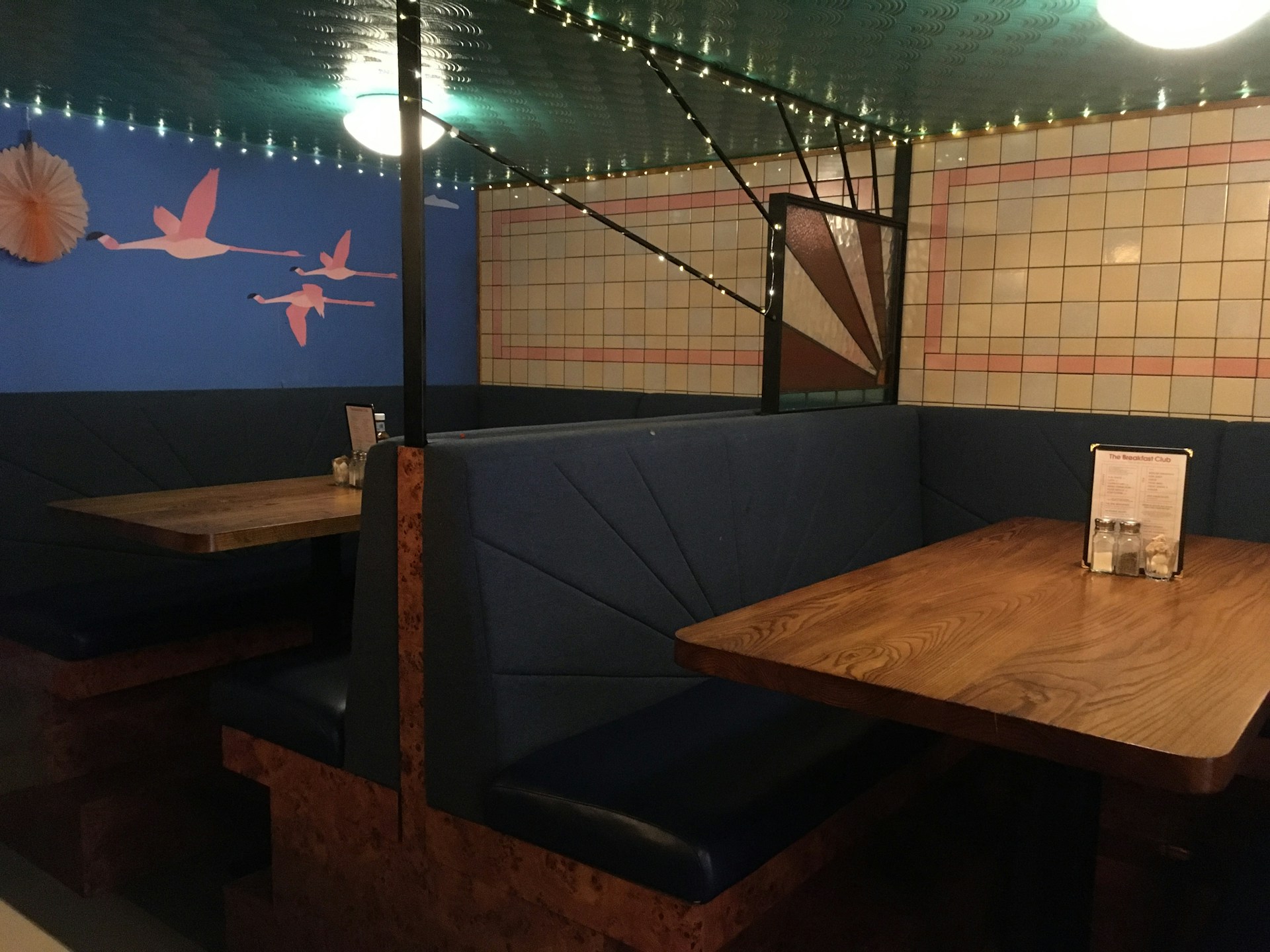 The cozy interior of The Fat Swan Restaurant featuring hand-lettered menus on wooden boards, soft golden lighting, and a coral red accent wall with a swan emblem.