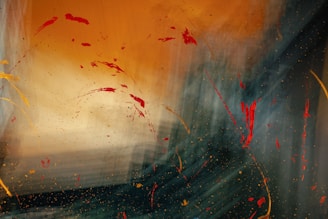 An abstract composition featuring a blend of warm and cool tones. Bold red splatters and strokes scatter across the canvas with a sweeping motion. The background transitions from a vibrant orange to darker, bluish shades, creating a dynamic fluidity.