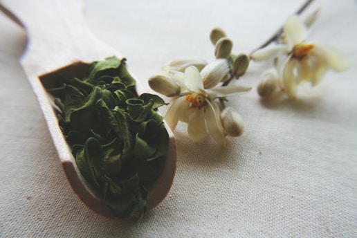 Close-up of vibrant moringa powder spilling from a rustic wooden spoon onto a natural linen cloth.