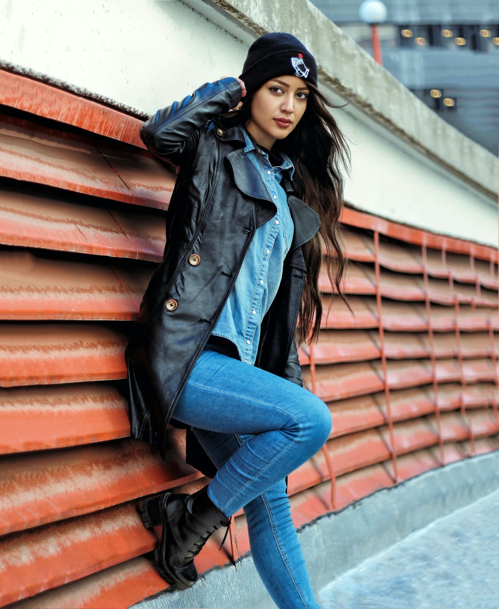 Mujer con chaqueta de cuero negro y jeans de mezclilla azul apoyados en la pared