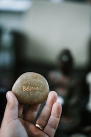 person holding brown stone with believe print