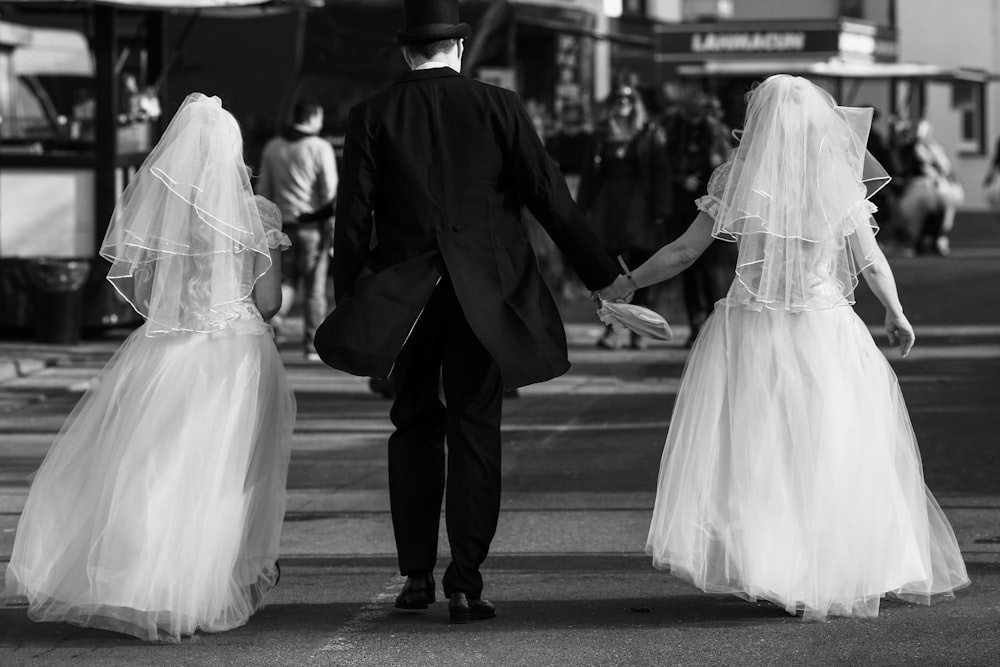 grayscale photography of two brides and groom walking on road