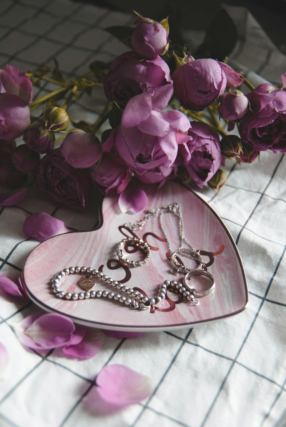 silver-colored rings and bracelet on plate with pink roses