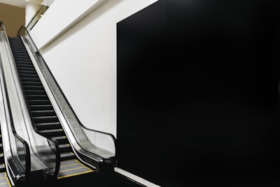 An indoor escalator with a sleek, modern design ascends next to a plain wall, creating a minimalistic and geometric composition.