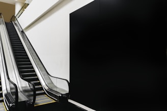 An indoor escalator with a sleek, modern design ascends next to a plain wall, creating a minimalistic and geometric composition.
