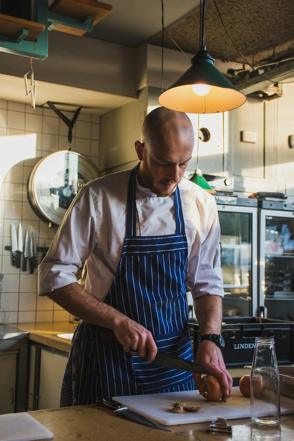 man wearing blue and white pinstripe apron slicing meat in kitchen