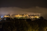 Night shot of a Gothic castle illuminated by warm torchlight against a dark sky.