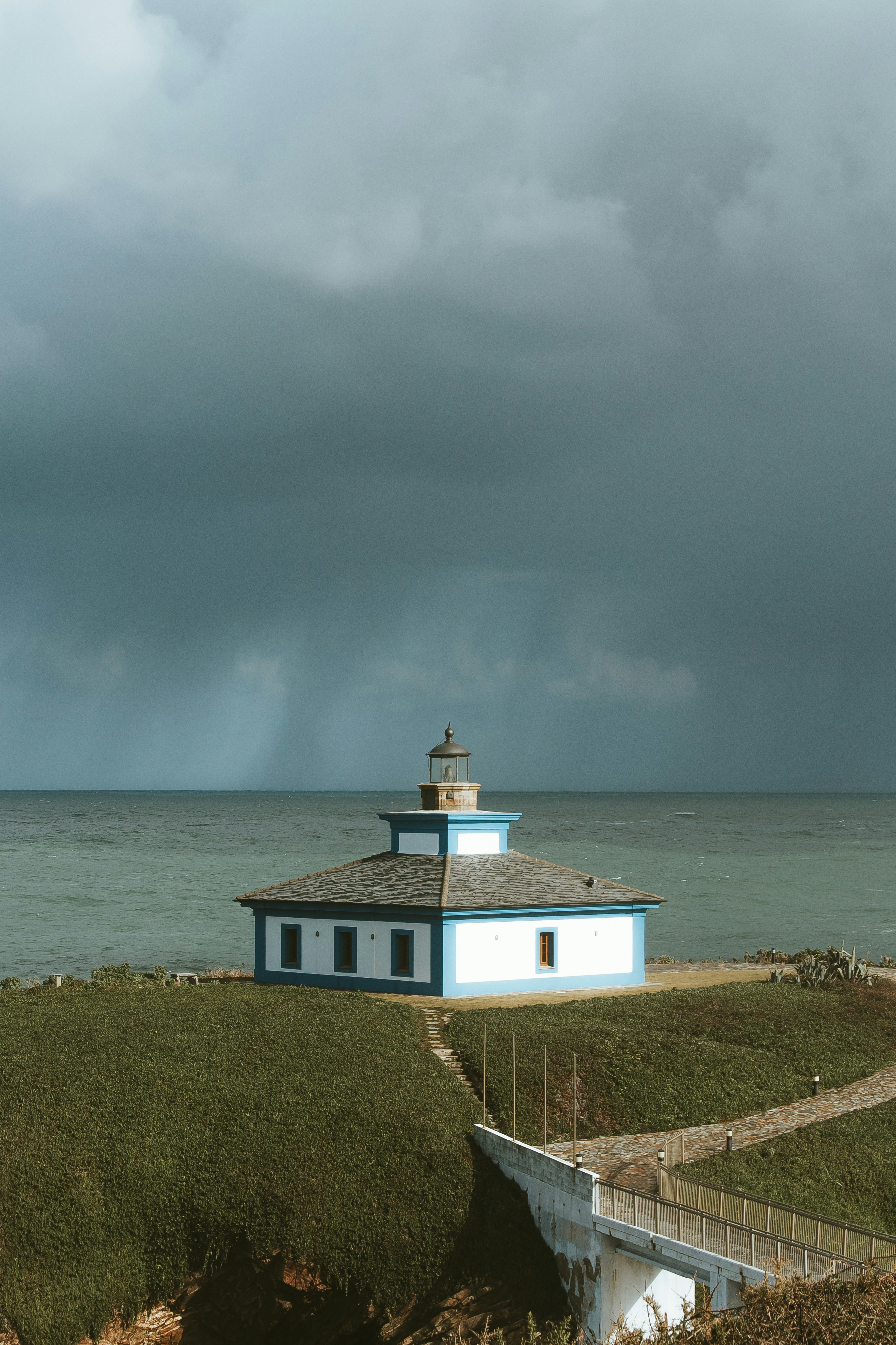 white and blue concrete house on hill near body of water under cloudy sky