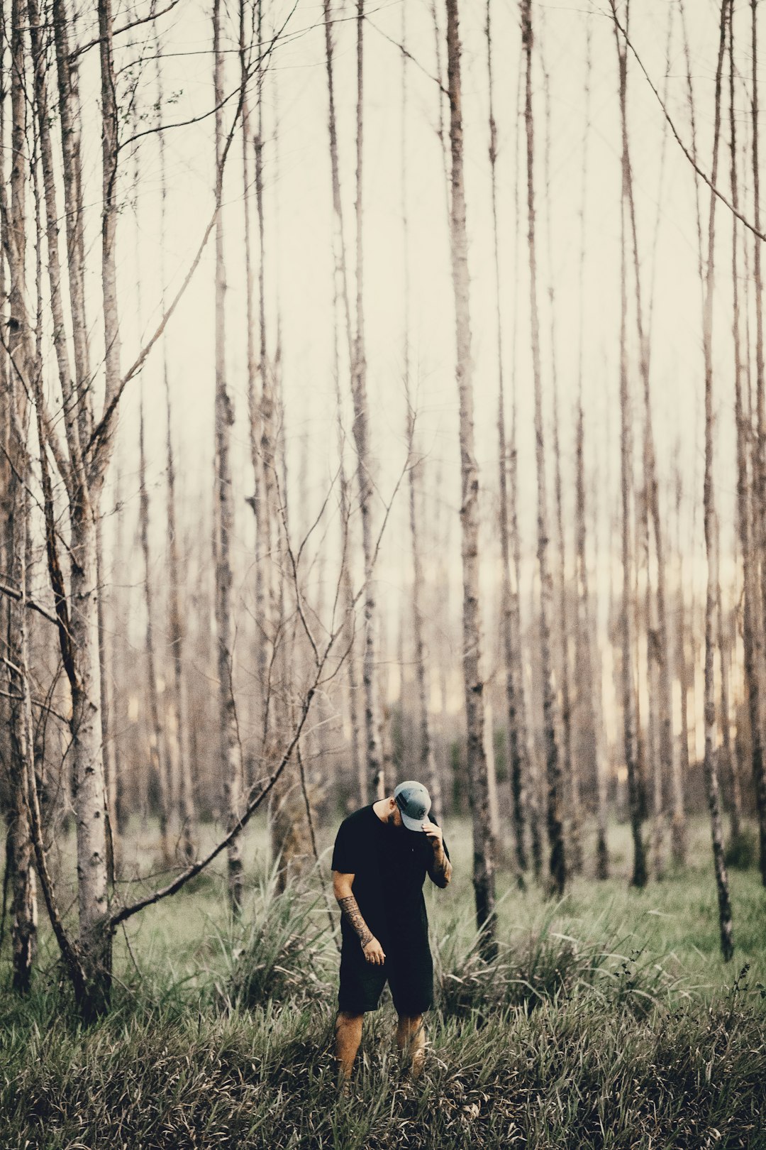 man wearing black shirt and shorts standing beside bare trees