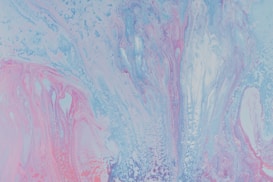A vibrant abstract painting featuring a fluid mix of pastel colors. Swirling patterns of light blue, pink, and lavender create a dynamic and ethereal composition.