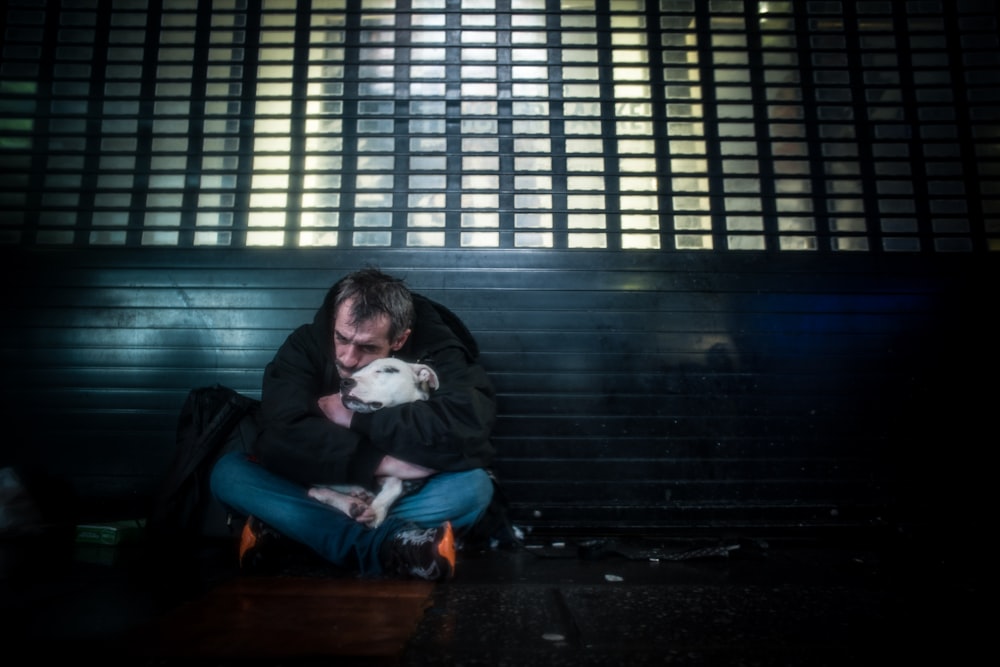 man hugging white dog while sitting on bench near wall