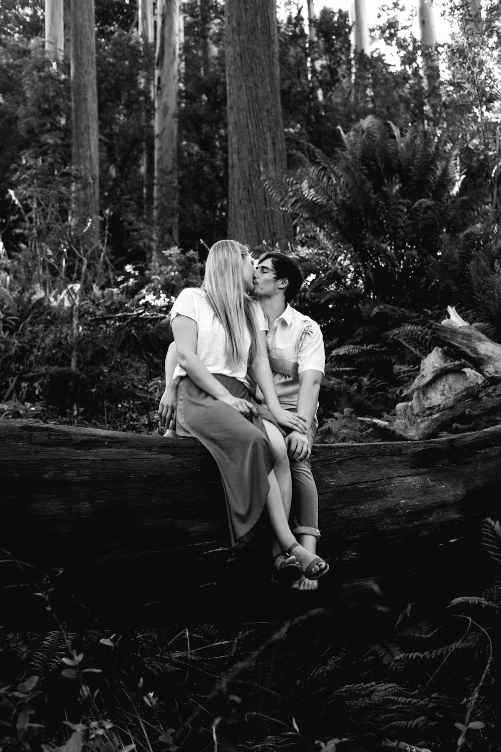 grayscale photography of man and woman kissing in forest