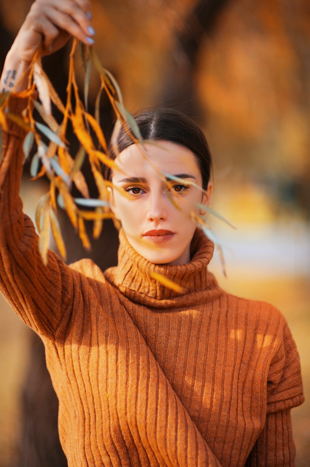 woman in brown turtleneck sweater holding tree leaves