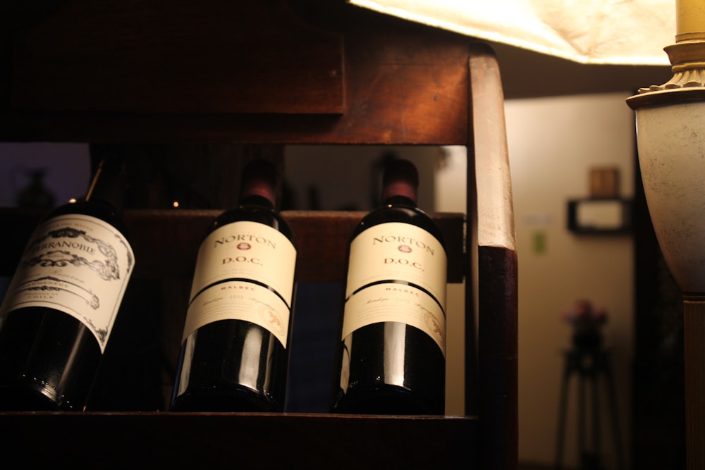 Tres botellas de vino de etiqueta blanca en estante de madera
