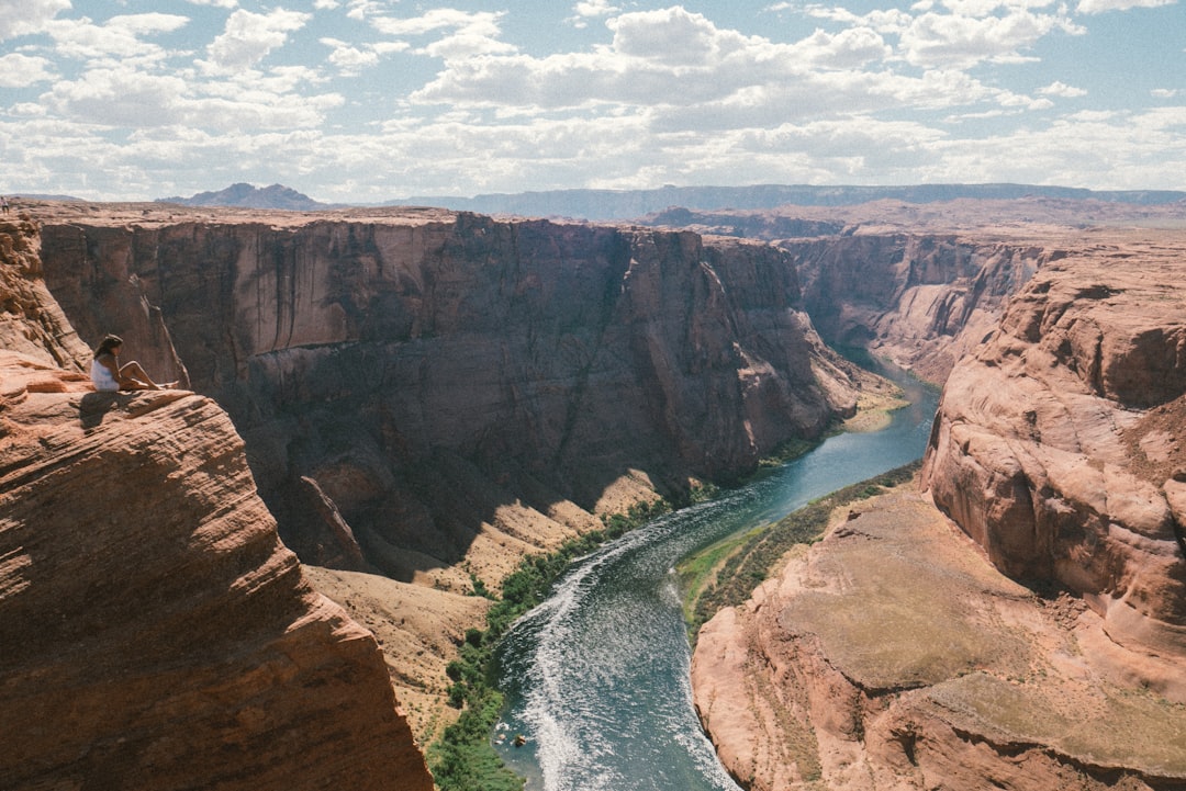 brown cliff near river, Girl sitting on the edge of a cliff near Horseshoe Bend in Arizona.