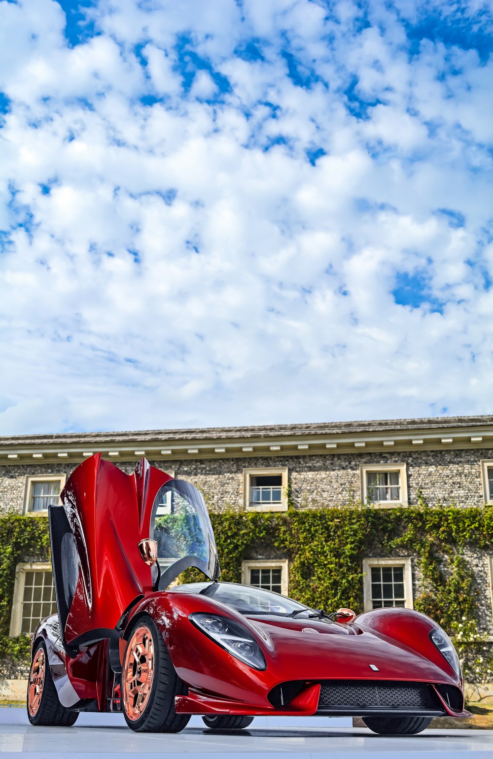 red sports coupe parked by stone-walled building at daytime