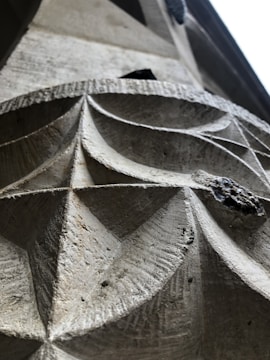 A close-up view of an intricately carved stone surface with geometric patterns. The texture and grooves in the stone are visible, showcasing precise craftsmanship and attention to detail. Natural light casts subtle shadows, highlighting the contours and depth of the carving.