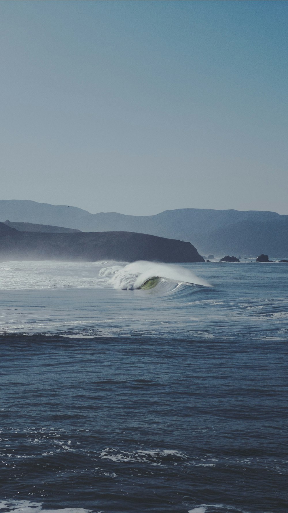 waves crashing near shore and cliff during daytime