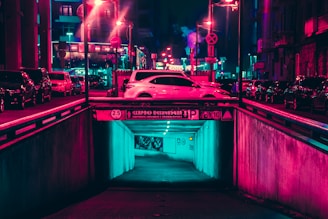 A neon-lit street scene at night with sleek cars parked under glowing signs, capturing the synth pop vibe of orldriftwave's car shows.