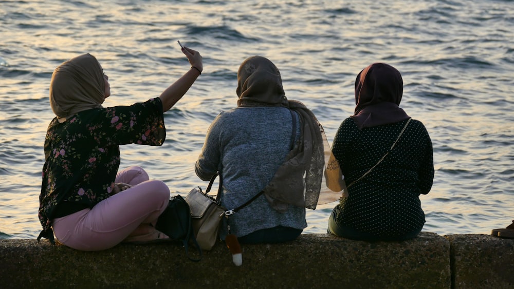 three women sitting beside body of water