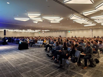 Wide shot of a corporate event hall filled with attentive attendees.