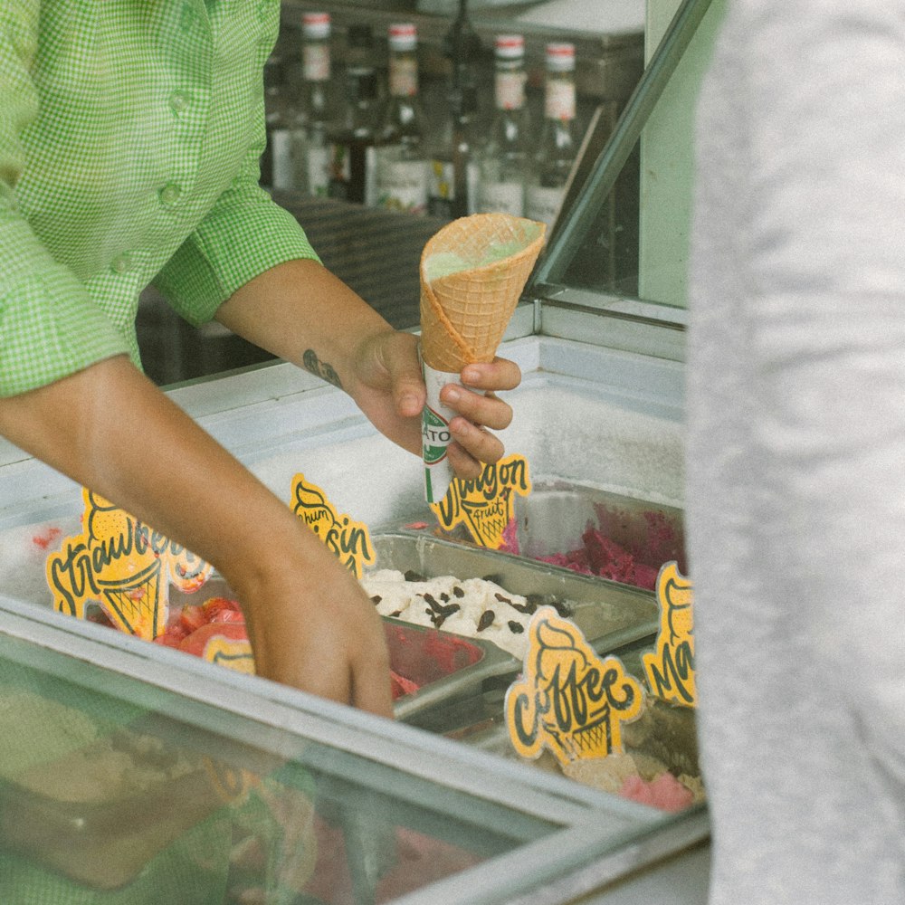 person holding ice cream cone and scooping ice cream in deep freezer