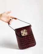 Close-up of a hand holding a compact crossbody bag against a vibrant urban backdrop.