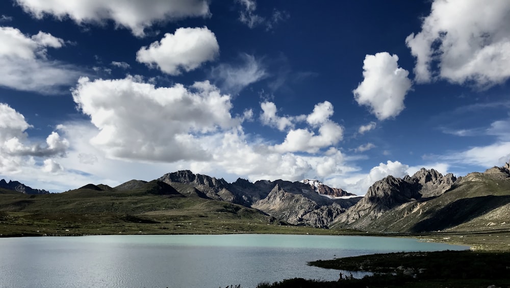 body of water near mountain under cloudy sky